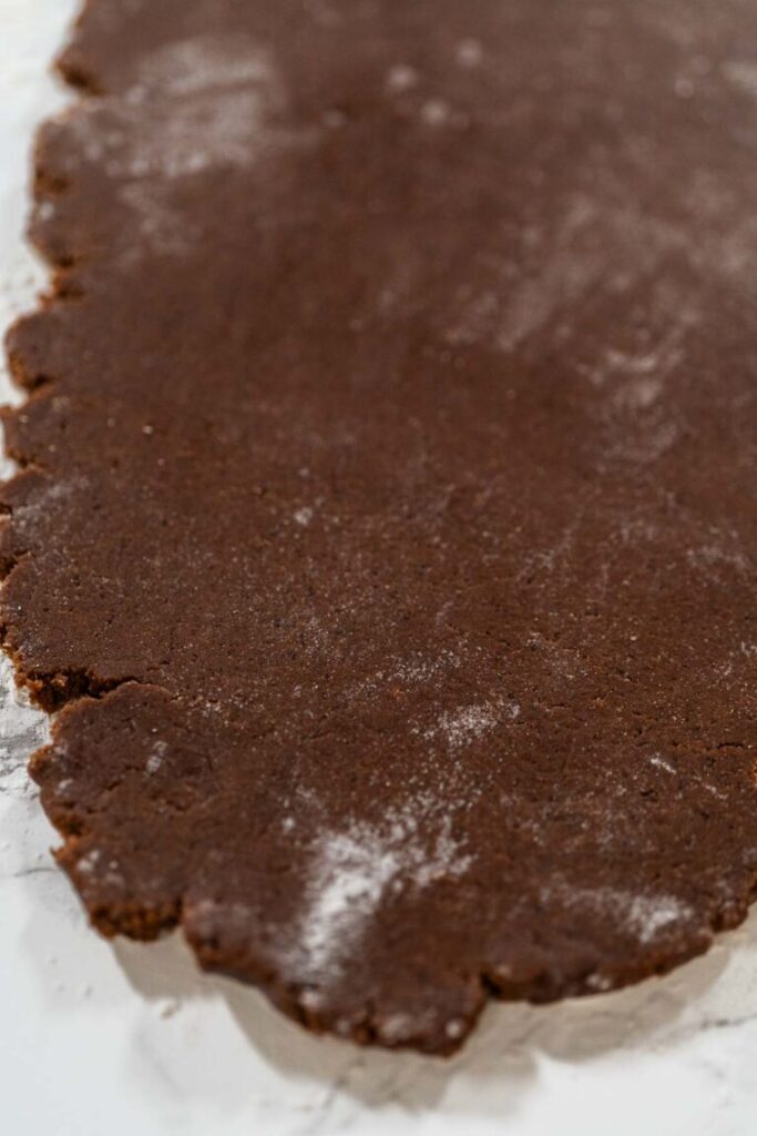 Rolled out chocolate-spiced gingerbread cookie dough on a floured marble surface ready for cutting shapes.