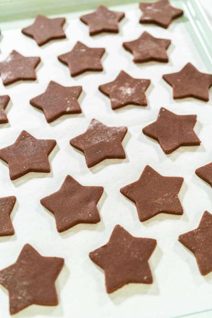 Multiple unbaked star-shaped chocolate-spiced gingerbread cookies arranged on a parchment-lined baking sheet.