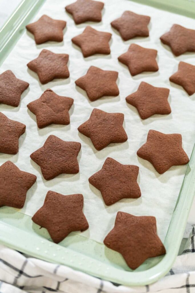 Freshly baked star-shaped chocolate-spiced gingerbread cookies cooling on a parchment-lined baking sheet.