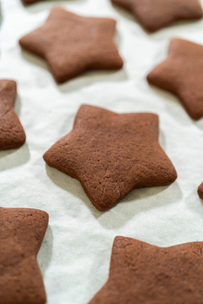 Close-up of a freshly baked star-shaped chocolate-spiced gingerbread cookie on a parchment-lined baking sheet.