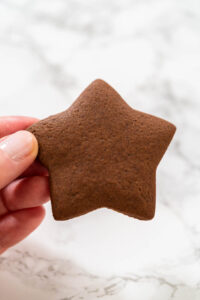 Hand holding a freshly baked star-shaped chocolate-spiced gingerbread cookie over a marble surface.