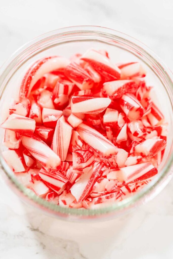 Close-up of crushed candy cane pieces in a glass jar on a marble surface.