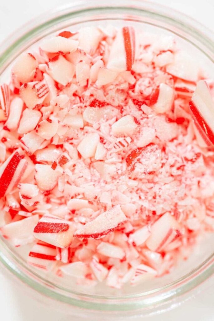 Close-up of crushed candy canes in a glass jar, showing red and white peppermint pieces for baking.