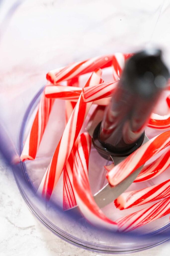 Whole peppermint candy canes in a food processor bowl, ready to be crushed for baking.