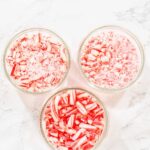 Three glass bowls filled with crushed candy canes in varying sizes, displayed on a white marble surface.