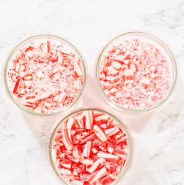 Three glass bowls filled with crushed candy canes in varying sizes, displayed on a white marble surface.