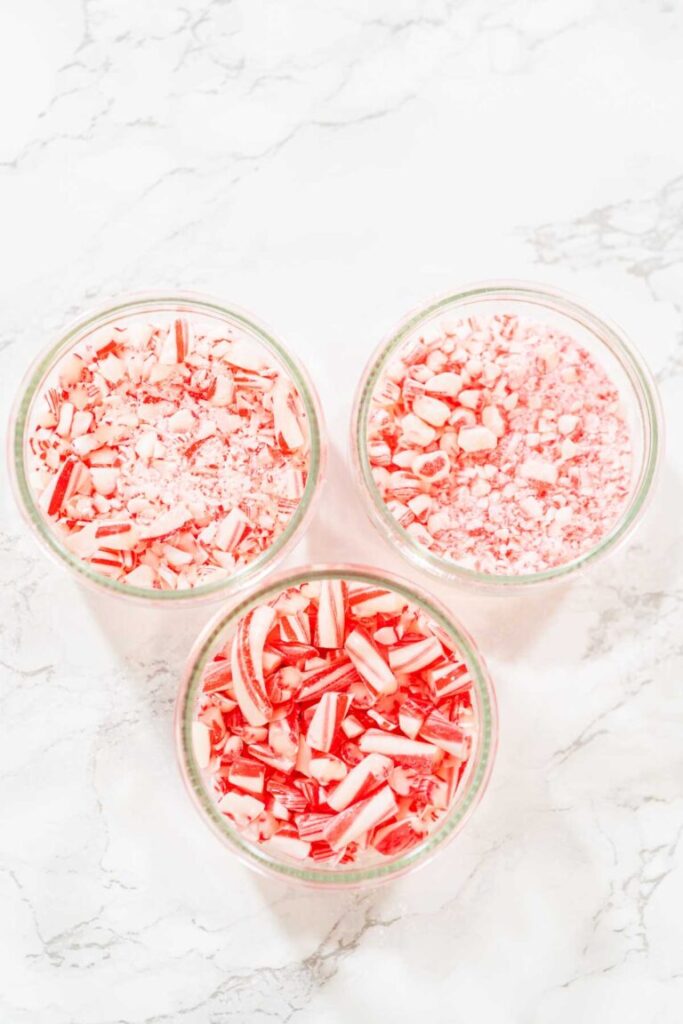 Three glass bowls filled with crushed candy canes in varying sizes, displayed on a white marble surface.