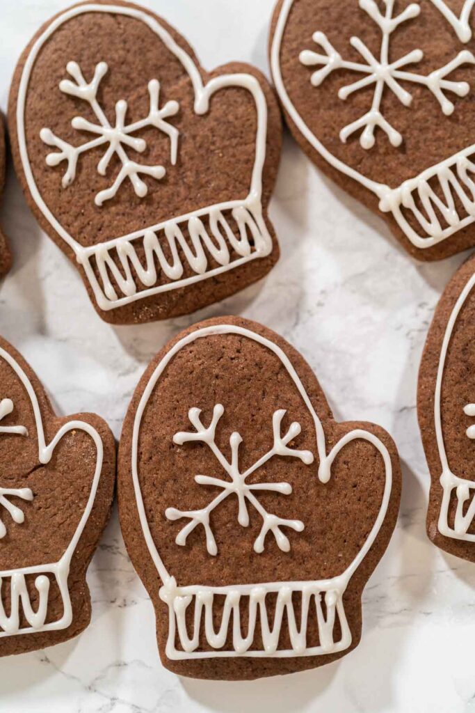 Chocolate mitten cookies decorated with white royal icing snowflakes and knit cuff designs for a festive winter look.