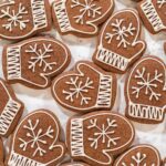 Overhead view of multiple mitten-shaped chocolate cookies decorated with white royal icing snowflakes and ribbed cuffs, arranged on a marble background.