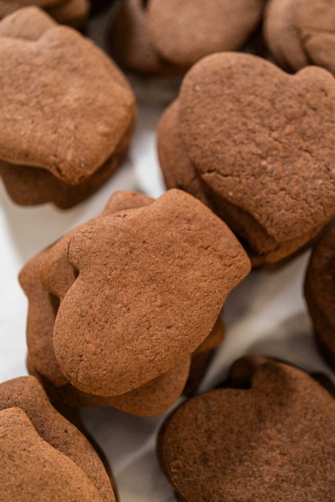 Stack of plain chocolate mitten-shaped cookies, freshly baked and ready to be decorated.