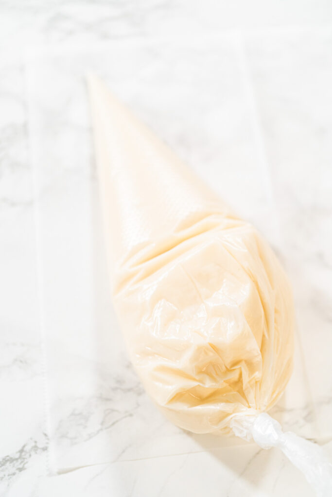 Close-up of a piping bag filled with white royal icing, resting on a marble surface, ready for cookie decorating.