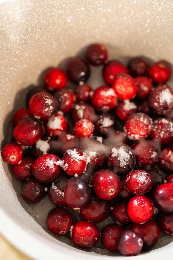 Close-up of fresh cranberries in a pot sprinkled with sugar, ready to be cooked down for cranberry puree.