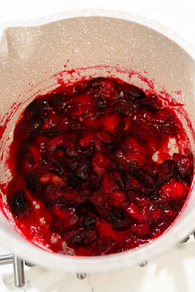 Cooked cranberries breaking down into a thick, chunky mixture in a saucepan, the first stage of making cranberry puree.