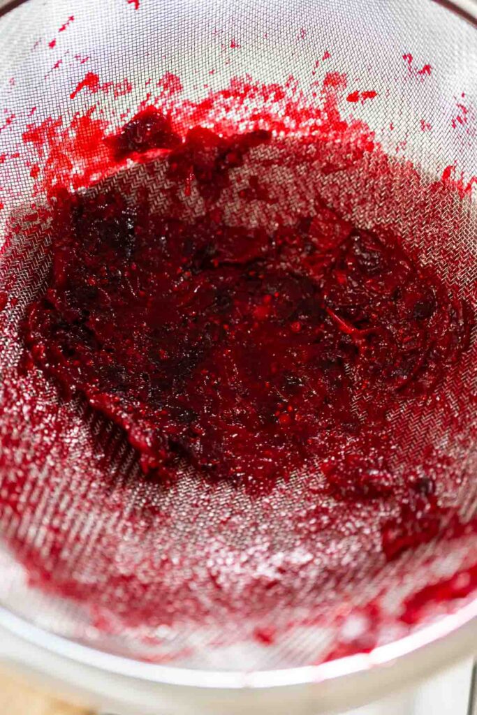 Strained cranberry solids left behind in a fine mesh sieve, showing the separation process for making smooth cranberry puree.