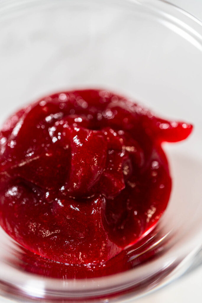 Close-up of smooth and glossy homemade cranberry puree in a glass bowl, ready to use for baking or frosting.