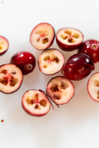 Halved fresh cranberries on a white cutting board, showing their pale interior and seeds, ready to be diced for recipes.