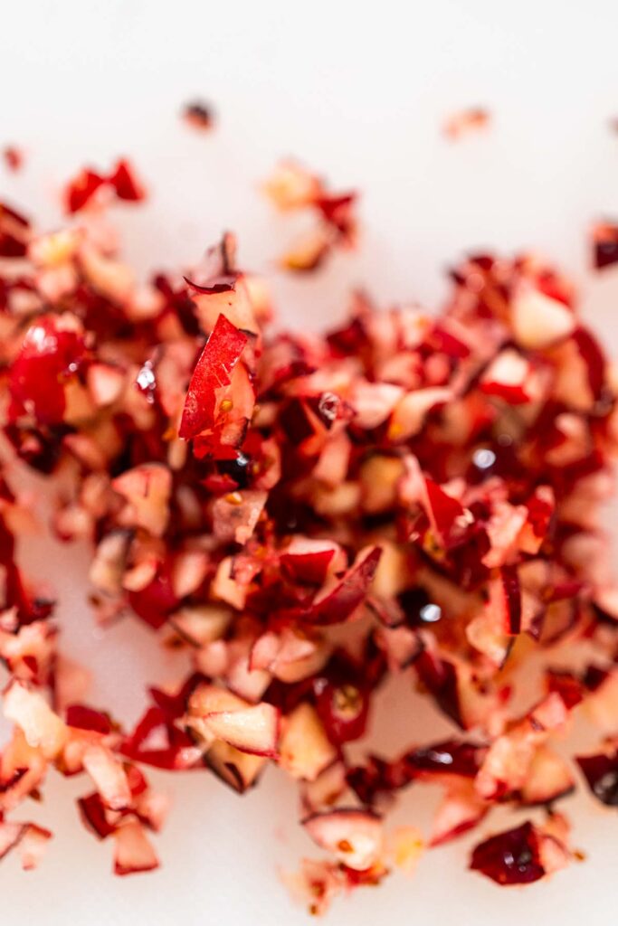 Close-up of freshly diced cranberries on a cutting board, showing small red and white pieces ready for baking or cooking.