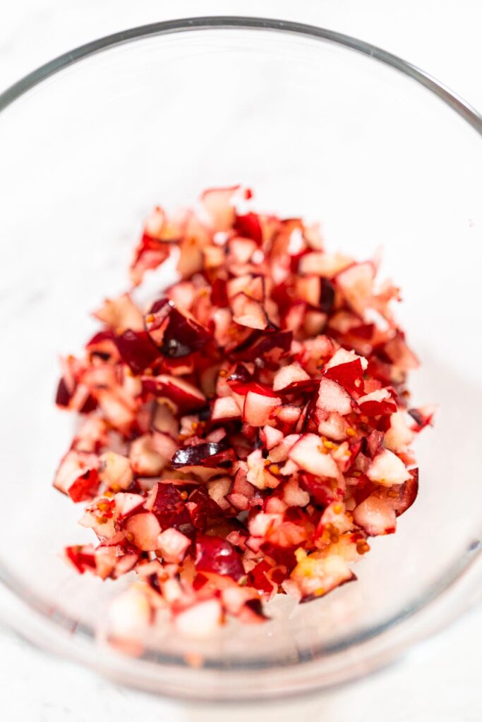Close-up of finely diced fresh cranberries in a glass bowl, showing their bright red skins and pale interiors.
