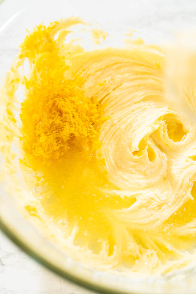 Creamed butter mixture with added lemon zest and juice in a glass bowl for lemon spritz cookie dough.