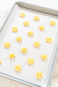 Freshly pressed lemon spritz cookies arranged on a parchment-lined baking sheet, ready to be baked.