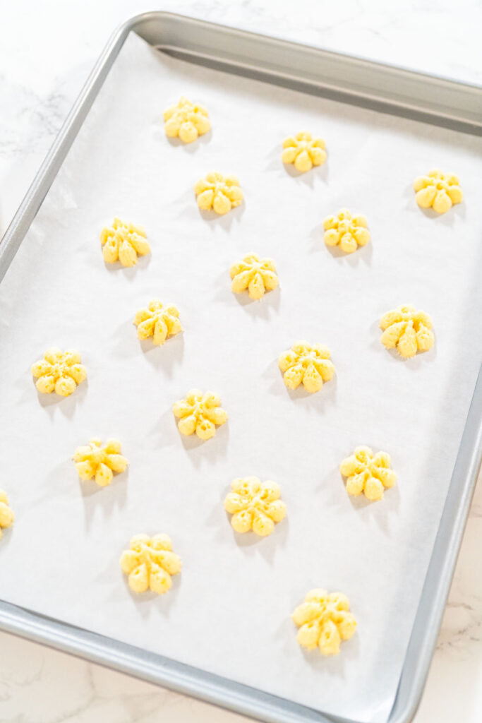 Freshly pressed lemon spritz cookies arranged on a parchment-lined baking sheet, ready to be baked.
