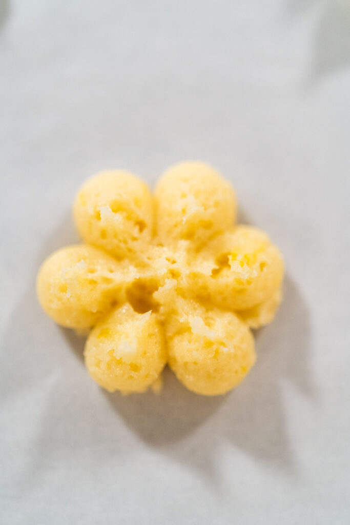 Spritz cookie press pressing flower-shaped cookie dough onto a parchment-lined baking sheet.
