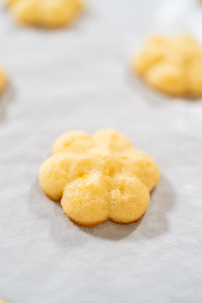 Close-up of a freshly baked lemon spritz cookie with golden edges on parchment paper.