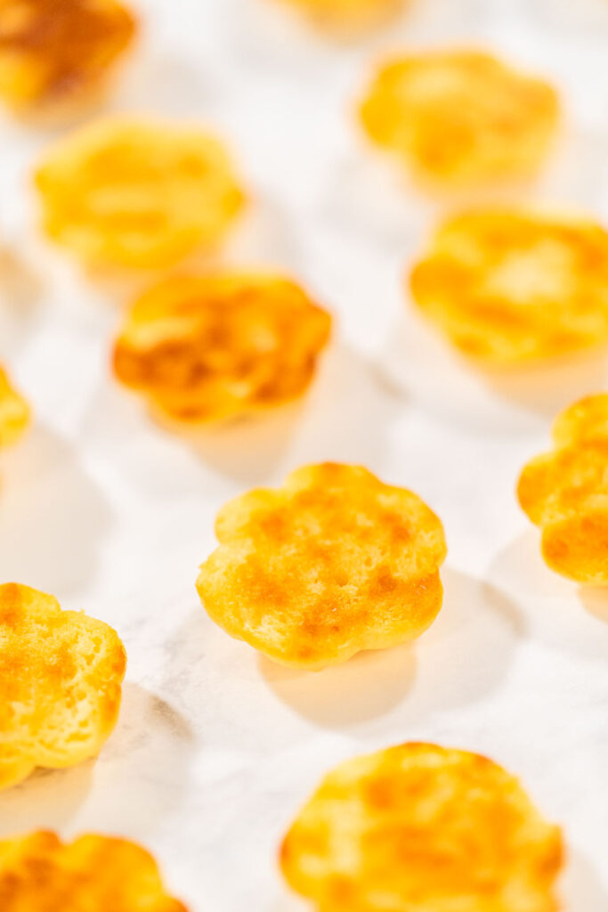 Baked lemon spritz cookies placed upside down on parchment paper, showing their golden browned bottoms.