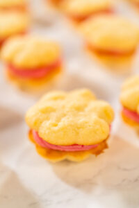 Lemon spritz sandwich cookie filled with cranberry buttercream, displayed on parchment paper.