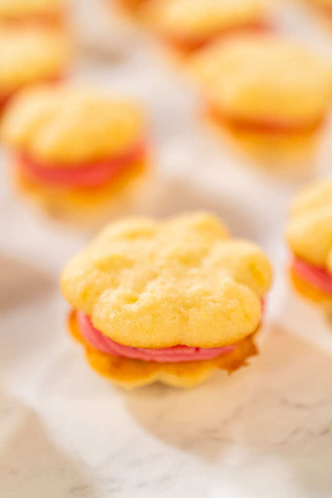 Lemon spritz sandwich cookie filled with cranberry buttercream, displayed on parchment paper.