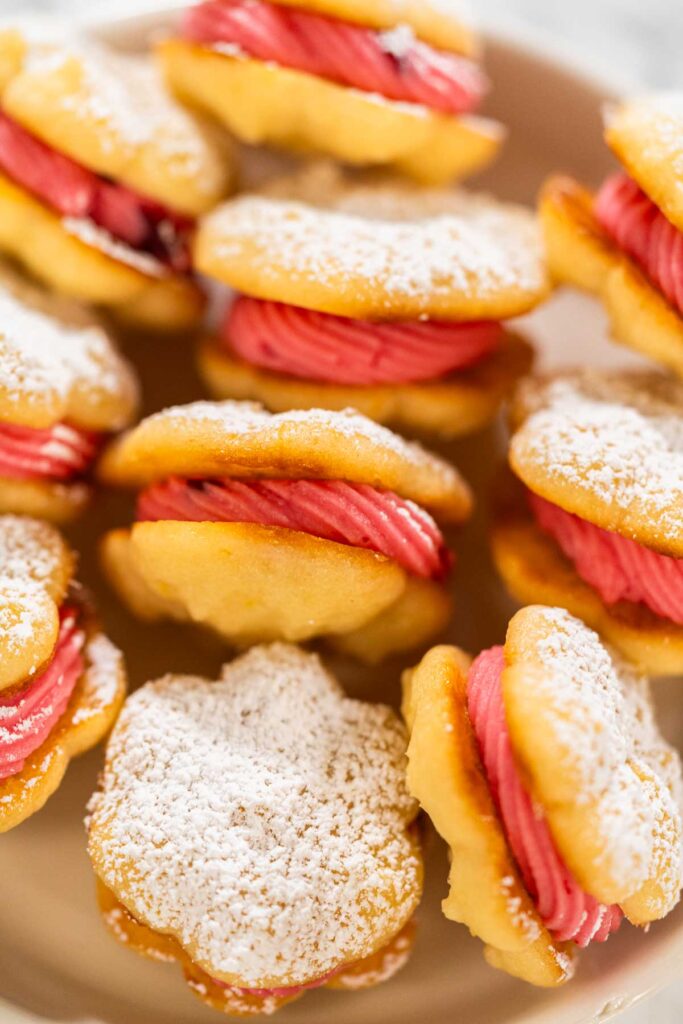 Stack of lemon spritz sandwich cookies with pink cranberry buttercream on a white platE.