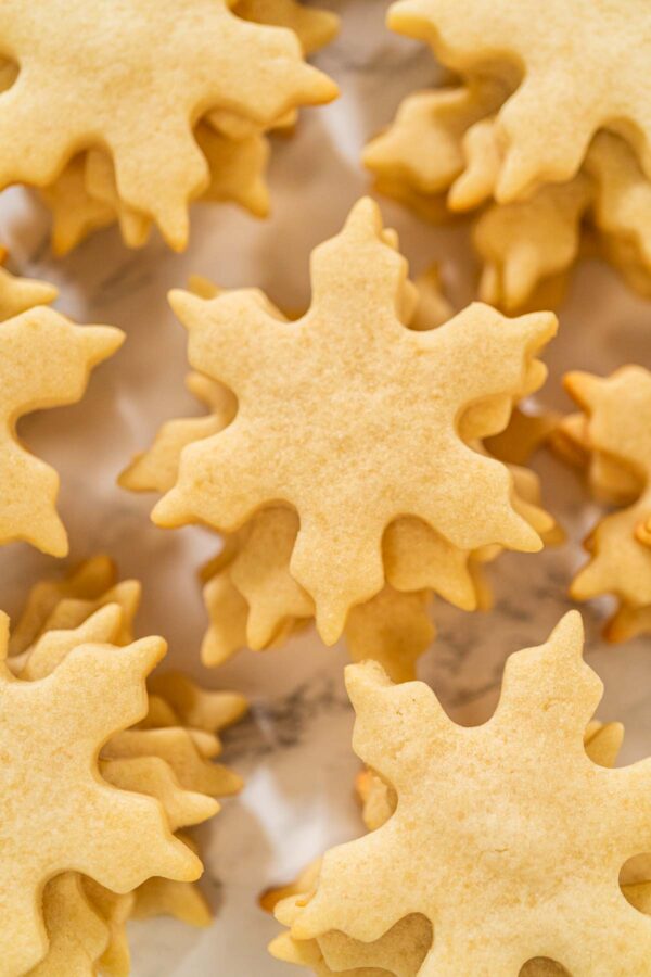 Plain snowflake-shaped sugar cookies stacked on parchment paper, ready for decorating or gifting