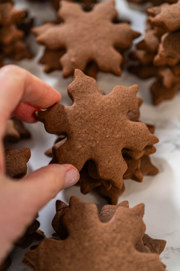 Close-up of a hand holding a chocolate snowflake cookie, showing its detailed shape and smooth surface before decorating with royal icing.