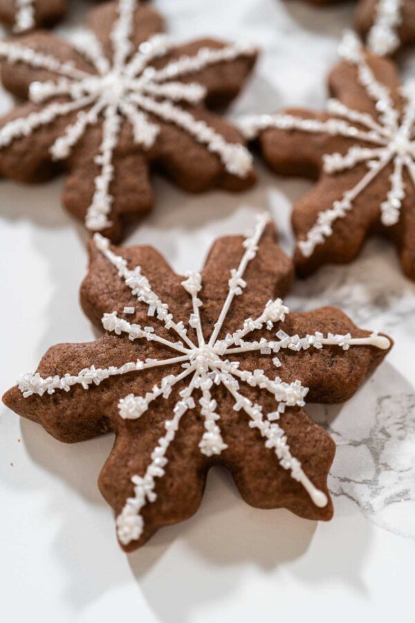 Close-up of a chocolate snowflake cookie decorated with white royal icing and sparkly sugar crystals, showing the intricate piped snowflake design.