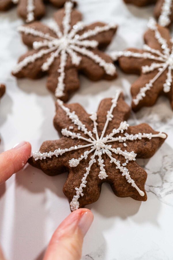 Chocolate snowflake cookie decorated with white royal icing in an intricate snowflake pattern and topped with sparkling sugar crystals—perfect for festive holiday treats.