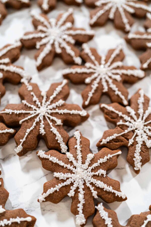 Overhead view of chocolate snowflake cookies decorated with white royal icing and sanding sugar, perfect for holiday gifting or festive dessert platters.