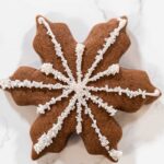 Close-up of a chocolate snowflake cookie decorated with white royal icing and sparkling sugar crystals, ideal for winter-themed holiday treats and Christmas dessert tables.