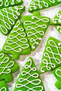 Green Christmas tree cookies decorated with white royal icing in swirl patterns, perfect for holiday baking and cookie boxes.
