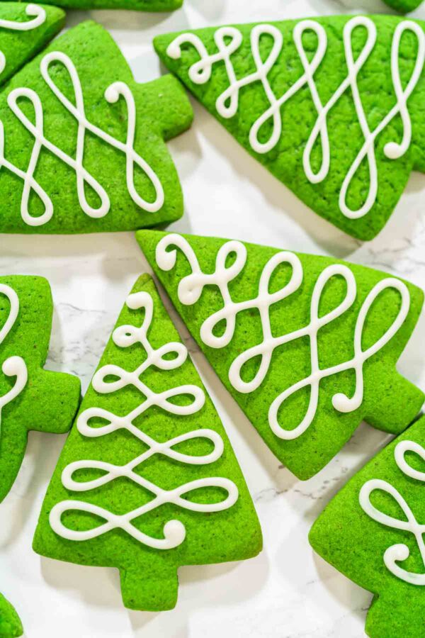 Bright green Christmas tree sugar cookies decorated with elegant white royal icing swirls, perfect for festive holiday baking and cookie gift boxes.