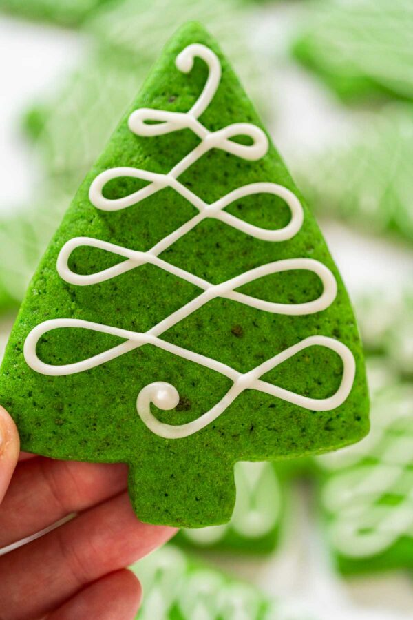 Close-up of a green Christmas tree cookie decorated with white royal icing swirls and a single sugar pearl, perfect for festive holiday cookie decorating.