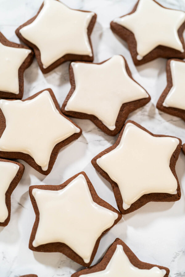 Flooded chocolate star cookies covered with smooth white royal icing, drying on a marble surface—perfect for holiday decorating or gifting.