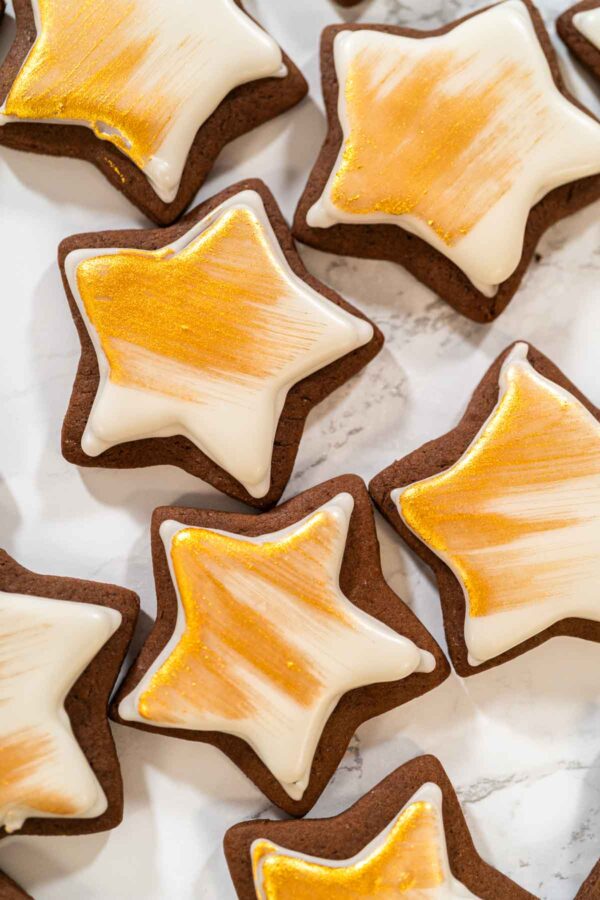 Close-up of chocolate star cookies decorated with white royal icing and brushed with edible gold dust—perfect for holiday cookie decorating or gifting.