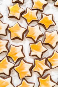 Overhead view of iced star cookies painted with edible gold luster dust, arranged on a marble surface—perfect for festive holiday cookie boxes or dessert tables.