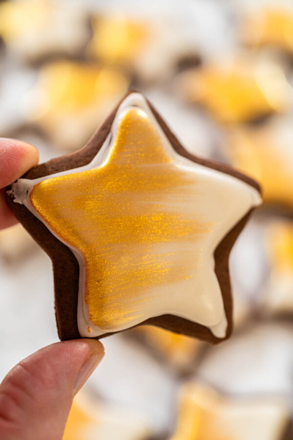 Chocolate star cookie decorated with smooth white royal icing and brushed with edible gold luster dust for a festive holiday treat.