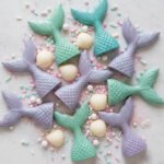 Colorful chocolate mermaid tails in shades of purple and teal arranged with pastel sprinkles and white chocolate seashells, illustrating chocolate mermaid tails for cupcake decorations.