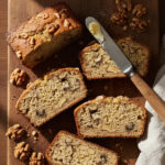 Sliced banana bread with walnuts on a wooden cutting board with a butter knife and scattered walnut pieces, illustrating simple banana bread with walnuts.